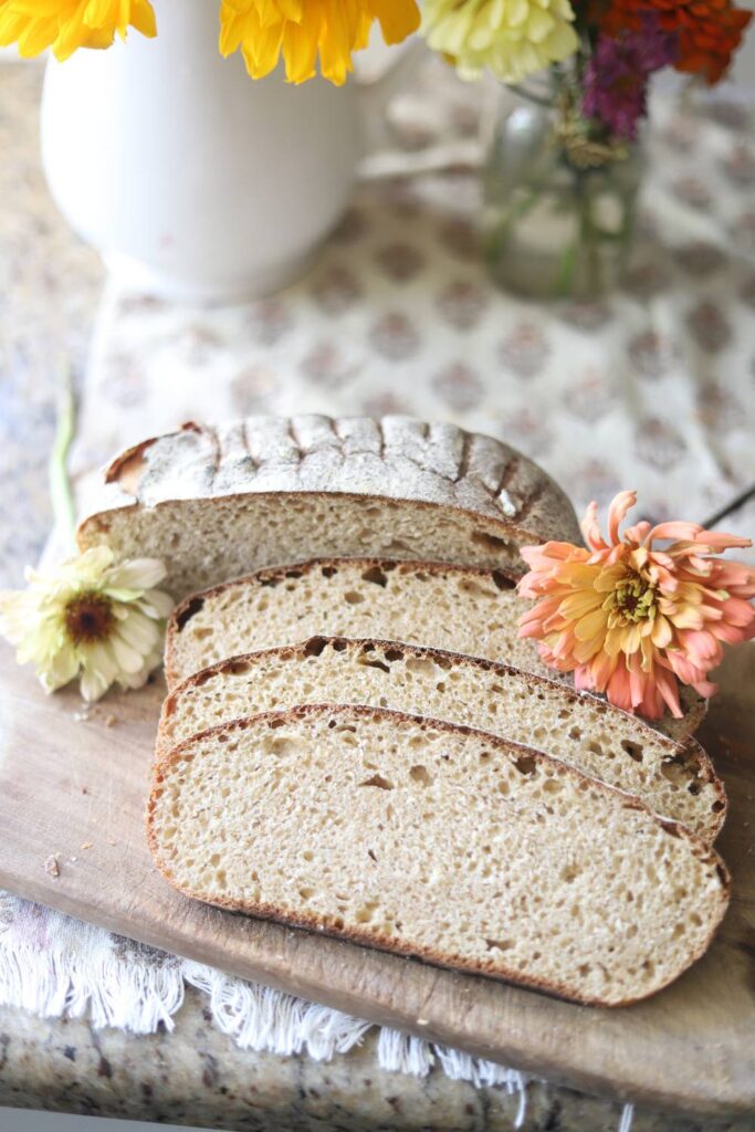 Rustic sourdough boule sliced on cutting board with fresh flowers