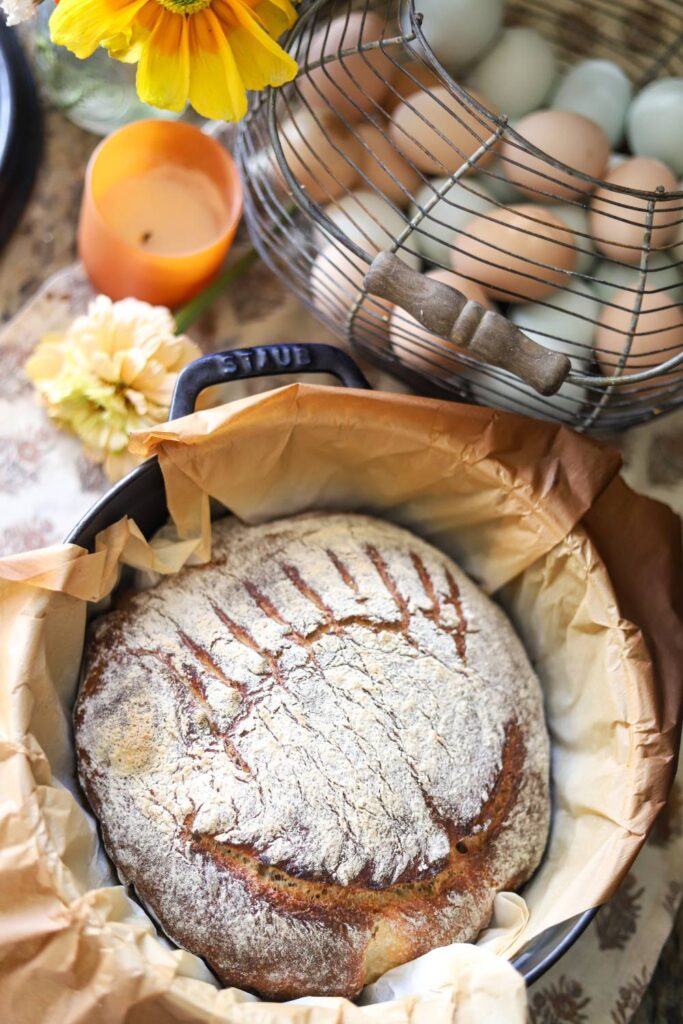 Flour-dusted sourdough boule cooling in Dutch oven with parchment paper