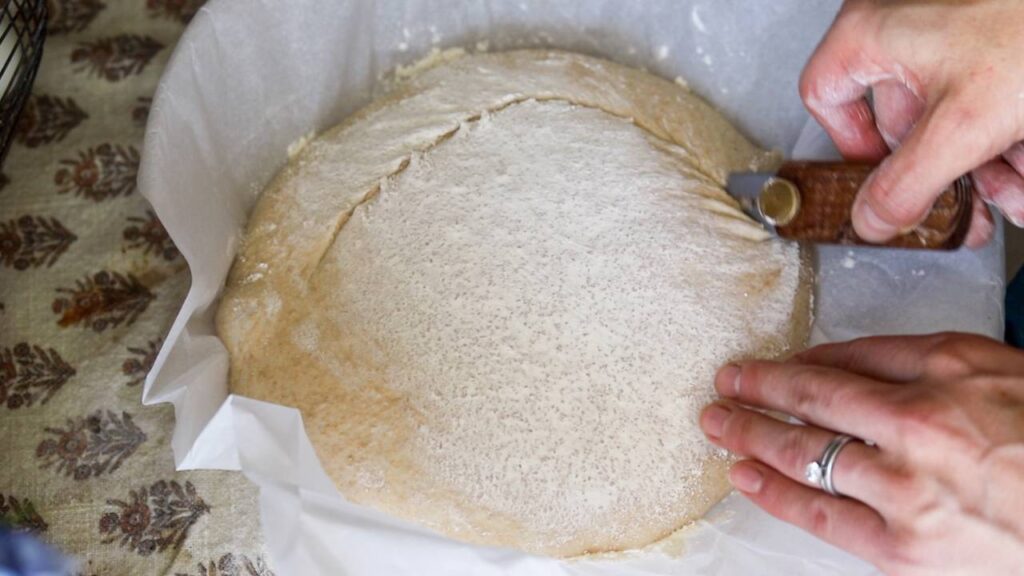 Hands scoring sourdough boule dough before baking