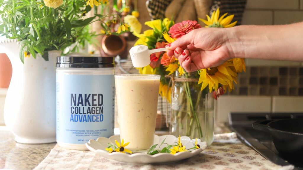Hand adding scoop of collagen powder to smoothie next to collagen container and flowers