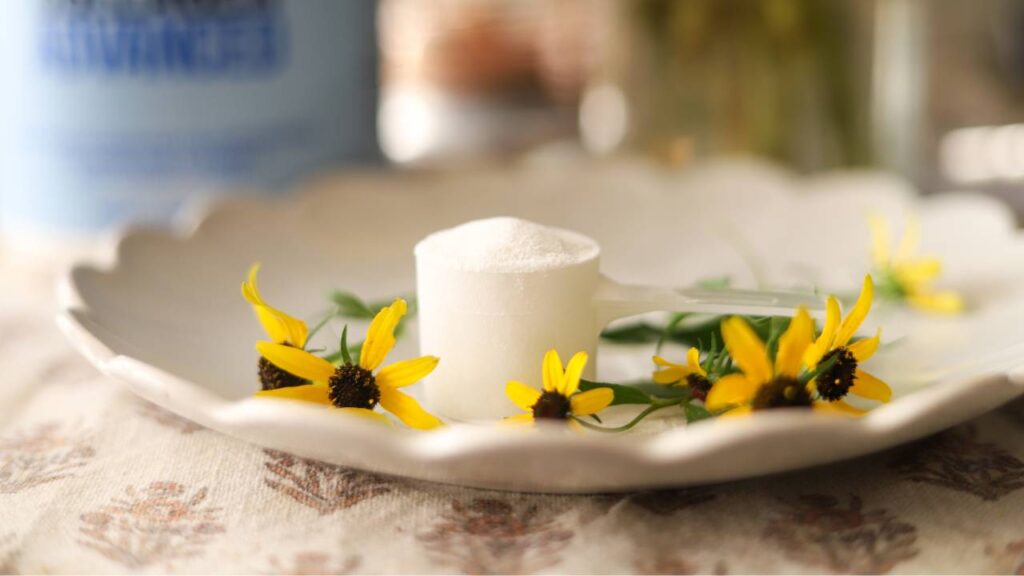 Close-up of scoop of collagen powder on plate with yellow flowers