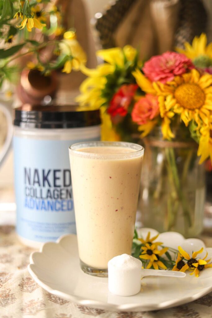 Glass of smoothie on plate with scoop of collagen powder and flowers