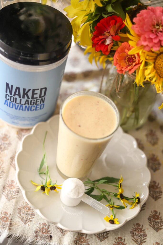 Overhead shot of smoothie, collagen container, scoop, and flowers on counter