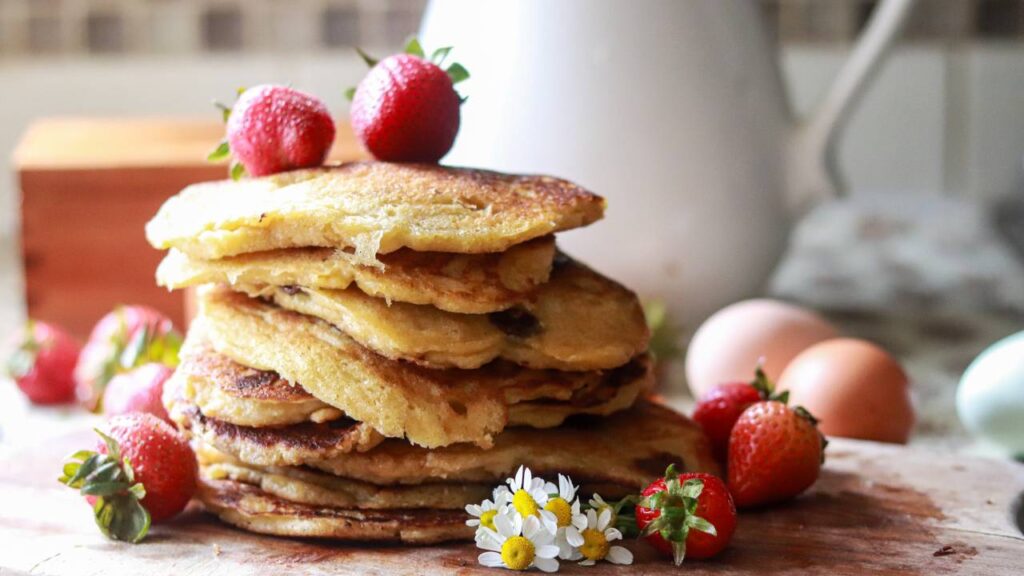 pile of sourdough pancakes on a cutting board with strawberries garnished around it and on top of the pancakes.
