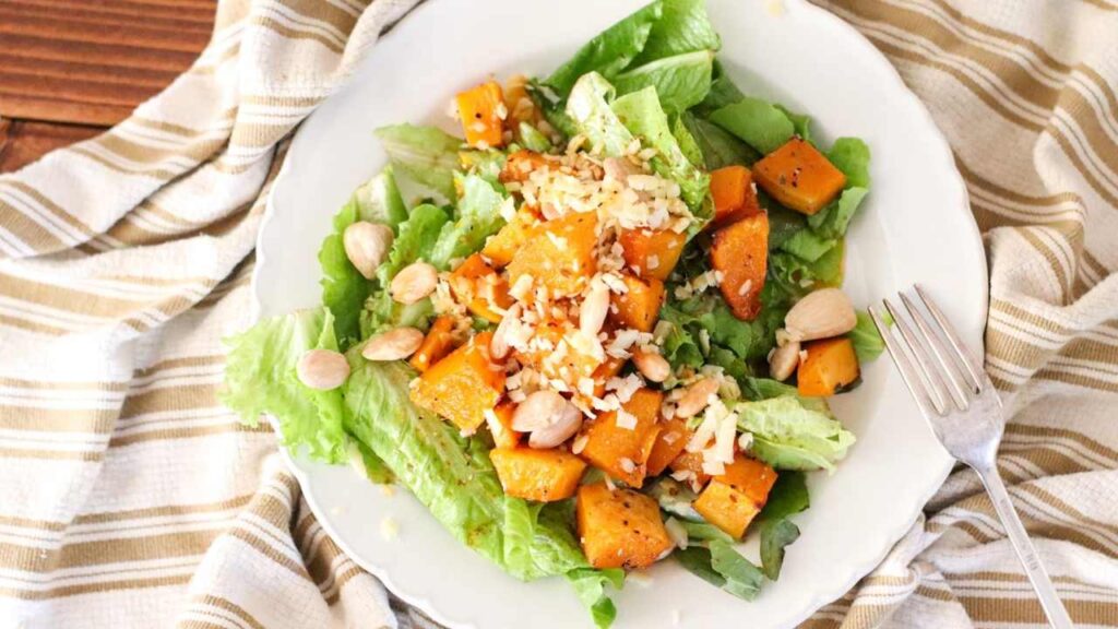 plate of fresh salad with butternut squash, almonds, and shredded cheese on top.