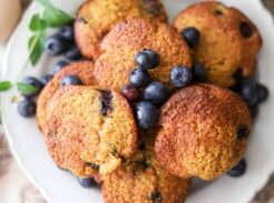 plate of fresh whole grain blueberry muffins with cornmeal with blueberries garnished around the plate and on top of the muffins.