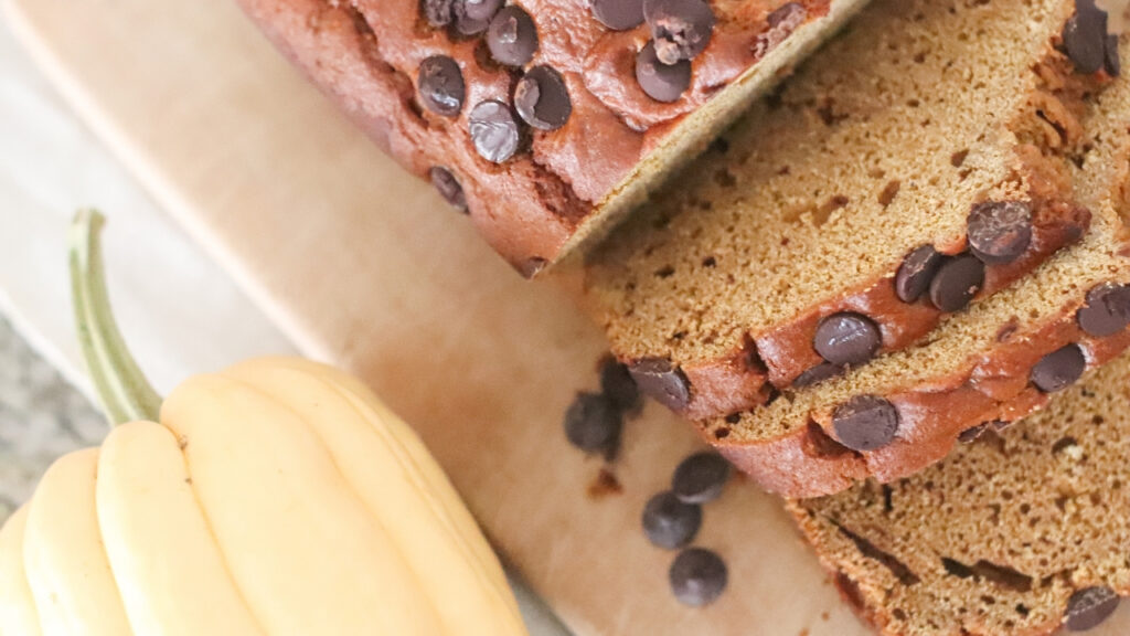 cut up pumpkin bread with chocolate chips on top with a squash sitting nearby in the background.