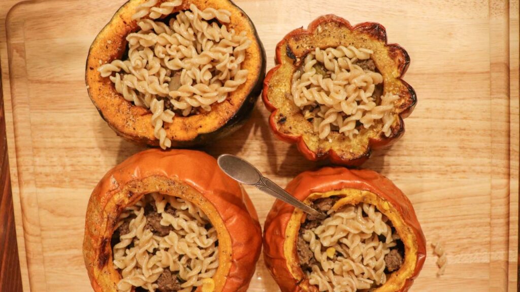 four squashes cut in half sitting on a wooden cutting board with a cooked pasta and meat mix inside.