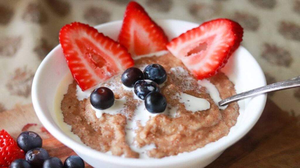 bowl of freshly milled cream of wheat with cream, blueberries, and strawberries on top.