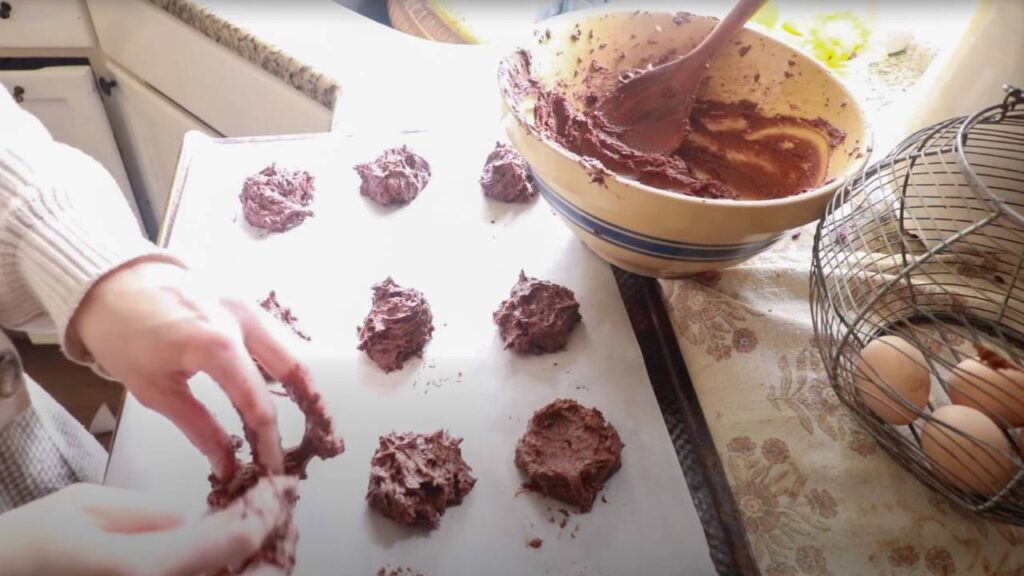 Hands shaping chocolate cookie dough on a baking sheet.