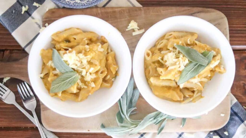 two bowls of butternut squash mac n cheese topped with shredded cheese and bay leaves