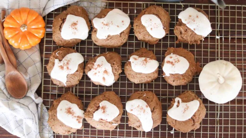rows of baked pumpkin cookies cooling on a wire rack with cream cheese icing on top.