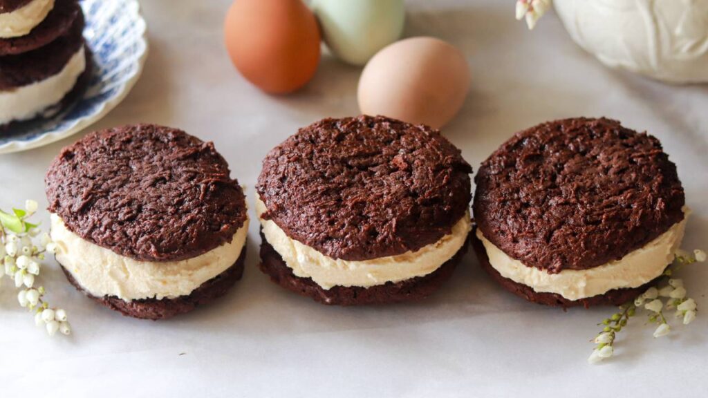 Three chocolate cookie ice cream sandwiches lined up on a counter.