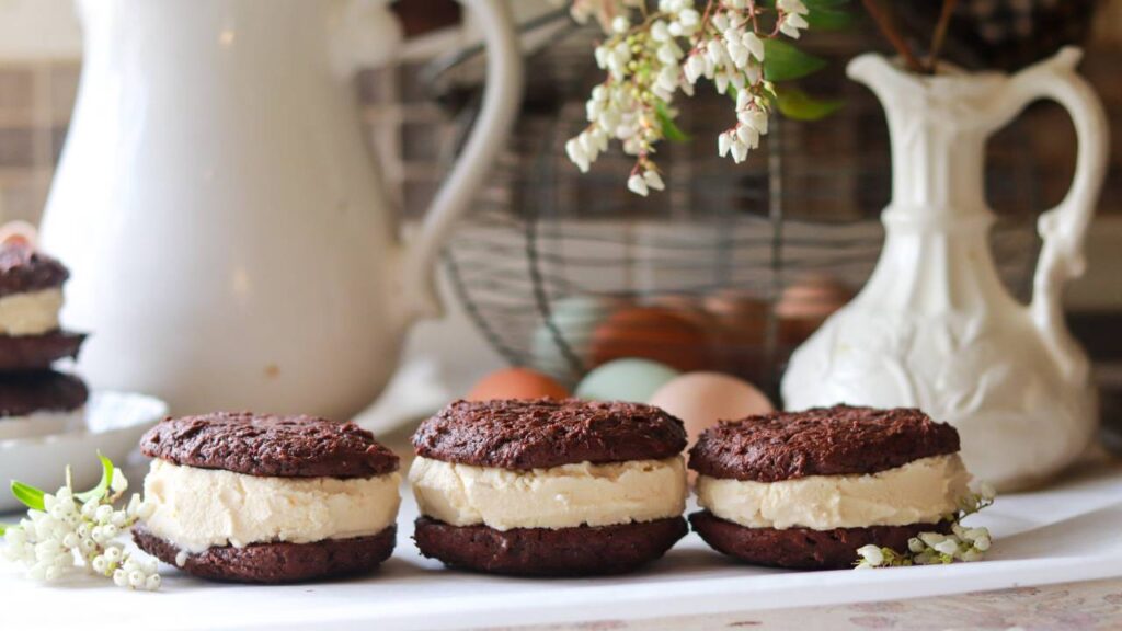 Three chocolate cookie ice cream sandwiches lined up on a counter.