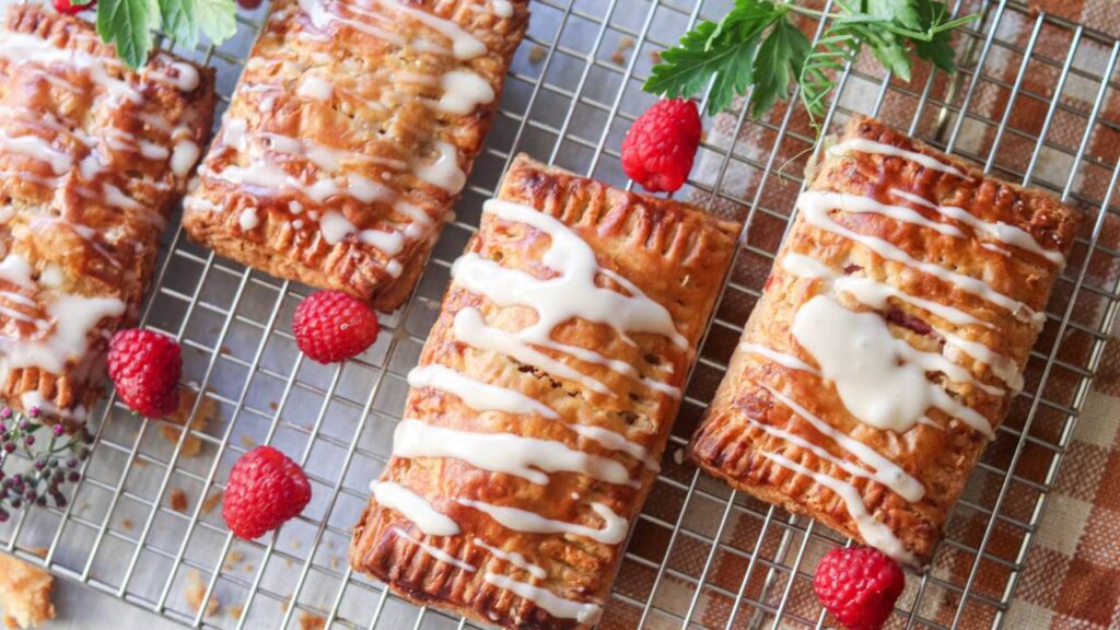 wire cooling rack with einkorn sourdough pop tarts with icing drizzled on top and raspberries garnished around them