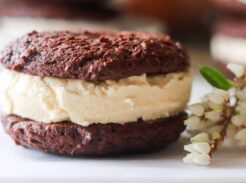 Close-up of a homemade chocolate cookie ice cream sandwich beside white flowers.