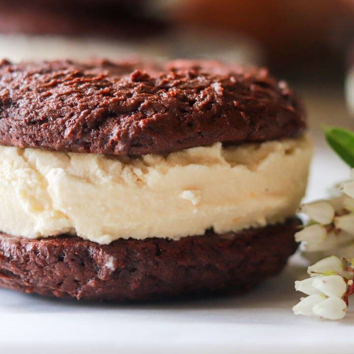 Close-up of a homemade chocolate cookie ice cream sandwich beside white flowers.