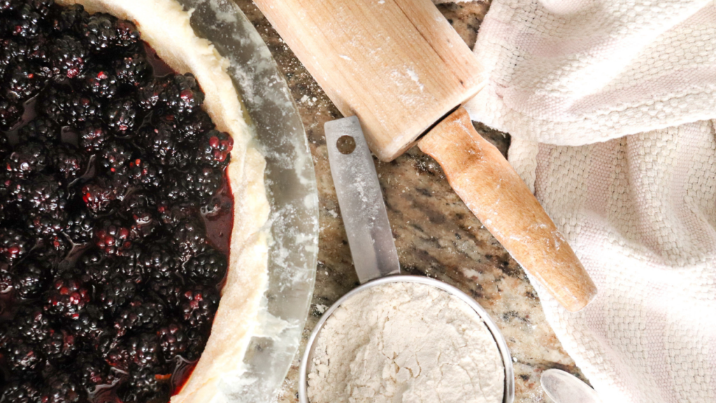 unbaked blackberry pie next to measuring cups and a rolling pin on a countertop