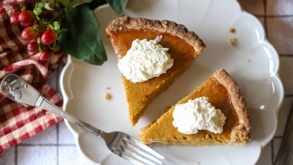 Overhead view of two pumpkin pie slices with whipped cream and a fork on the plate.