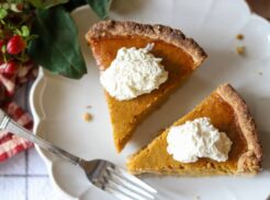Overhead view of two pumpkin pie slices with whipped cream and a fork on the plate.