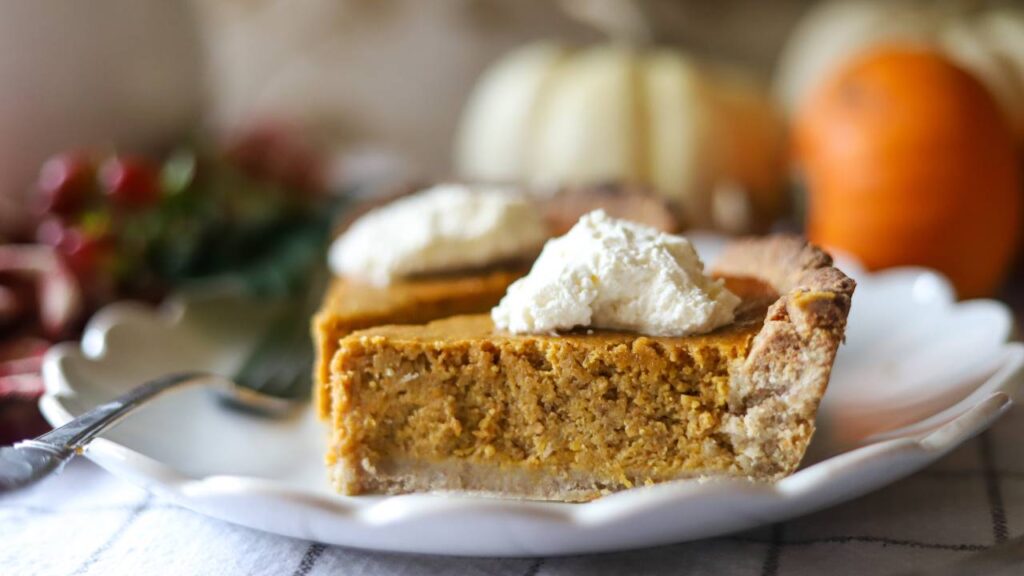 Close-up of two pumpkin pie slices with whipped cream on a white plate.