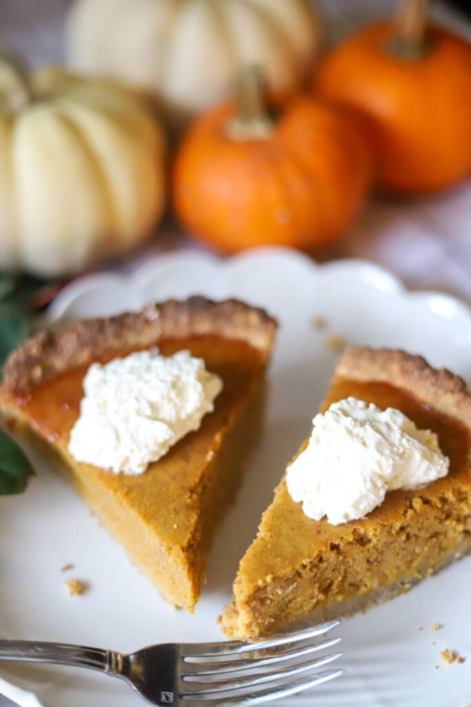 Pumpkin pie slices topped with whipped cream with small pumpkins in the background.