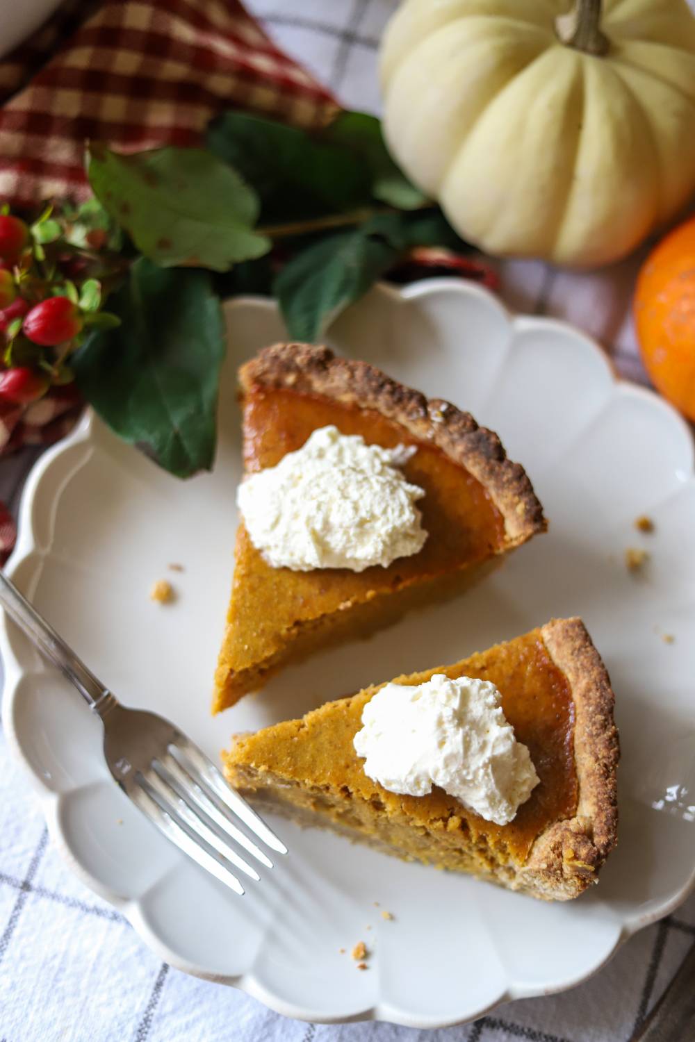 Two slices of pumpkin pie with whipped cream on a scalloped white plate overhead.