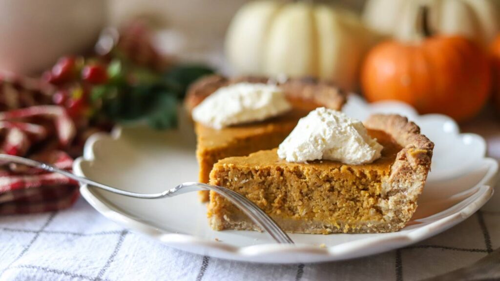 Side view of a slice of pumpkin pie with whipped cream on a white plate.