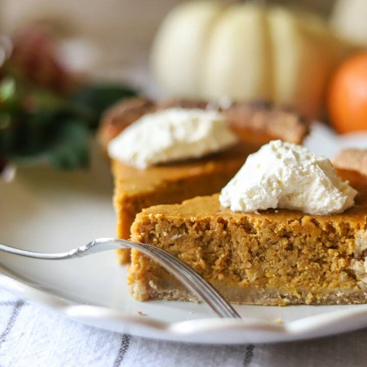 Side view of a slice of pumpkin pie with whipped cream on a white plate.
