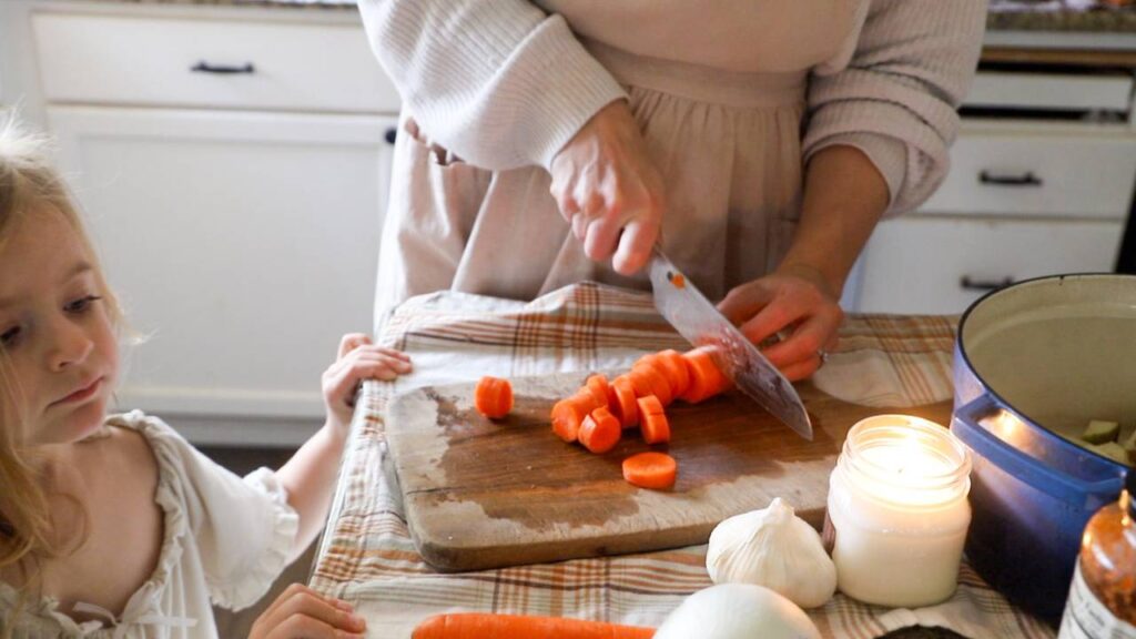 Woman slicing carrots on a cutting board with a child watching nearby.