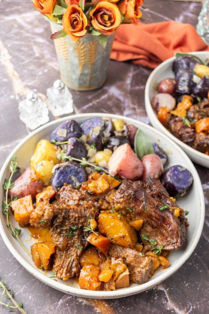 Two bowls of apple cider beef roast with mixed potatoes on a marble surface.