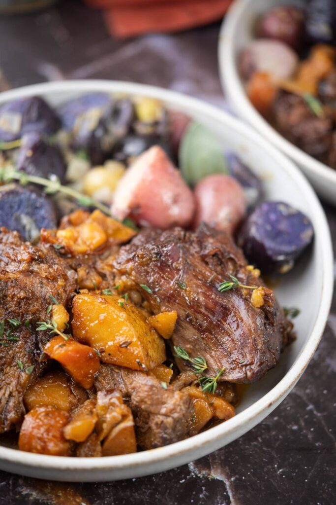 Plate of apple cider pot roast with mixed potatoes and carrots on a marble table.