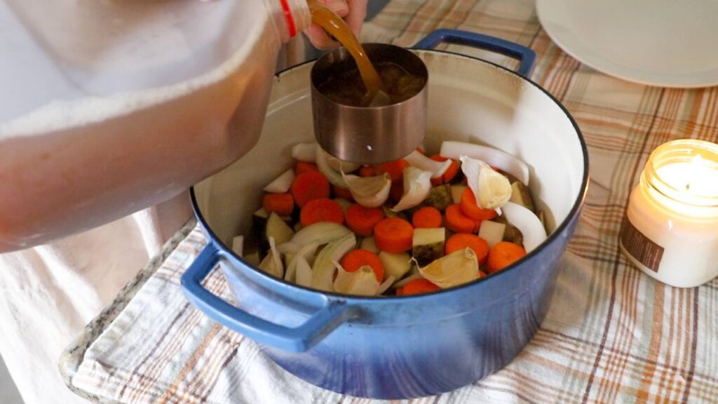 Pouring cider over chopped carrots, onions, and potatoes in a Dutch oven.