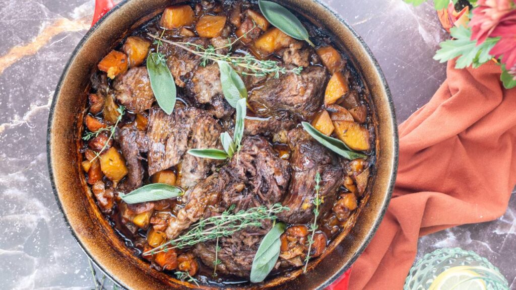Apple cider pot roast in a Dutch oven with carrots, potatoes, and fresh sage