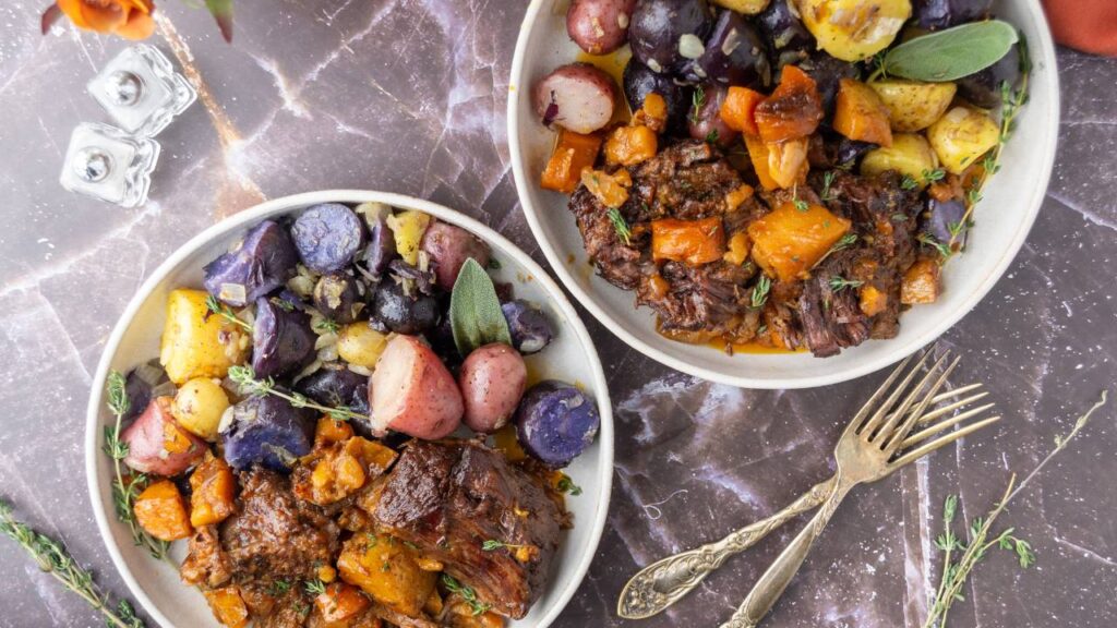 Two bowls of apple cider beef roast with mixed potatoes on a marble surface.