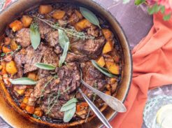 Dutch oven filled with apple cider pot roast, carrots, and potatoes topped with fresh herbs.