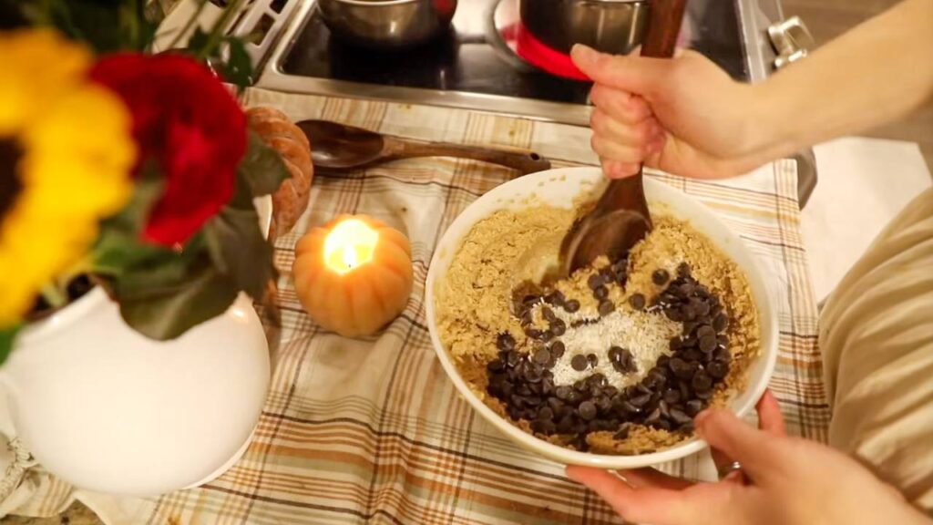 Stirring chocolate chips and coconut into pumpkin cookie dough in a mixing bowl on the kitchen counter