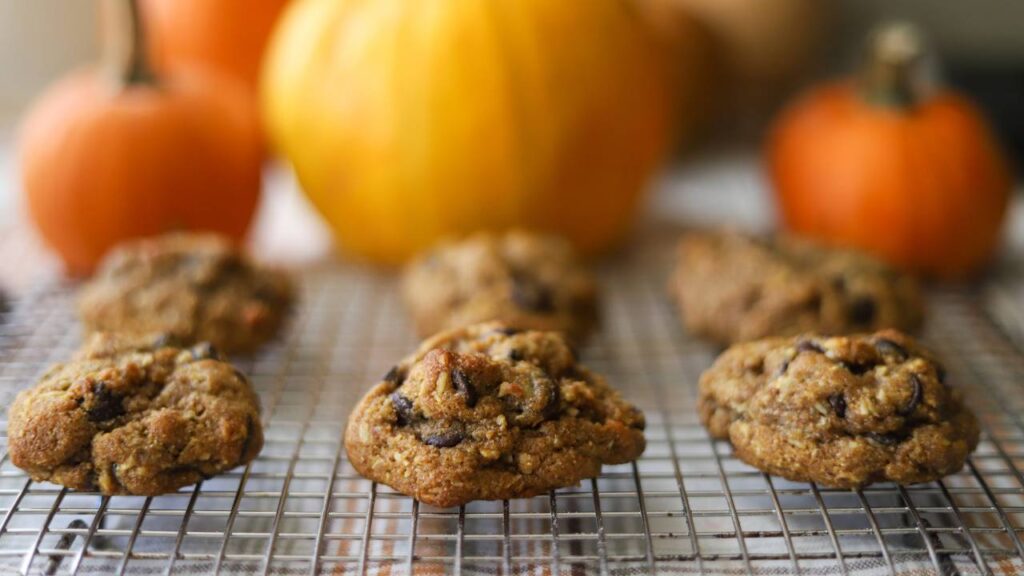 Pumpkin coconut chocolate chip cookies resting on a wire rack with pumpkins in the background
