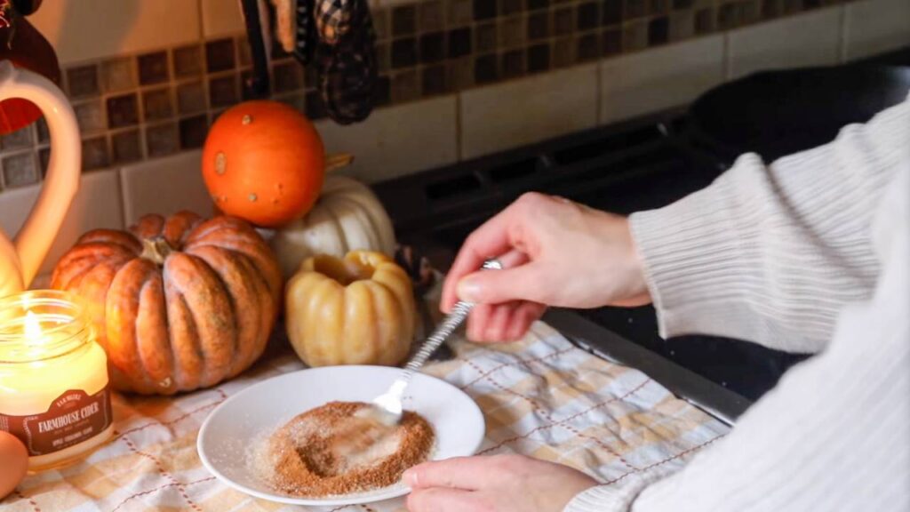 Coating baked apple cider donuts in cinnamon sugar