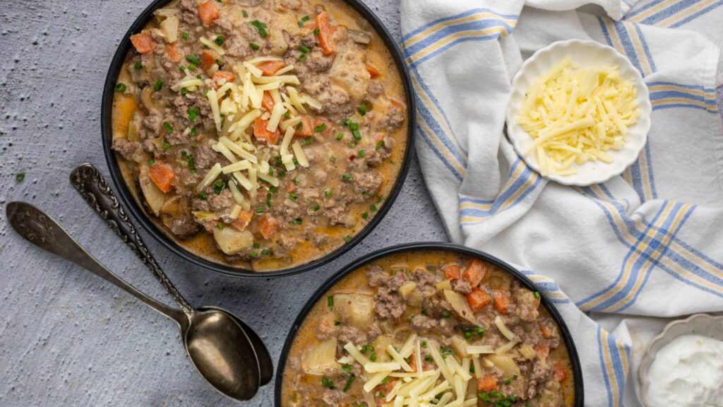 Two bowls of healthy cheeseburger soup with shredded cheese and chives