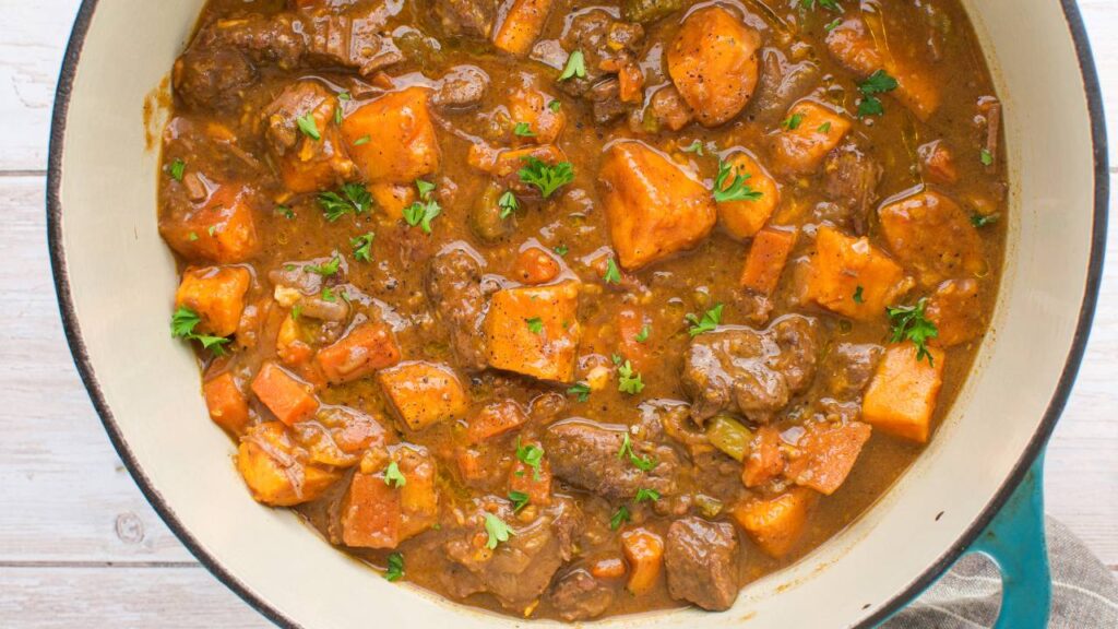 Pumpkin beef stew simmering in a Dutch oven with herbs on top