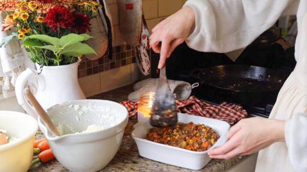 Layering meat filling into baking dish for shepherd’s pie