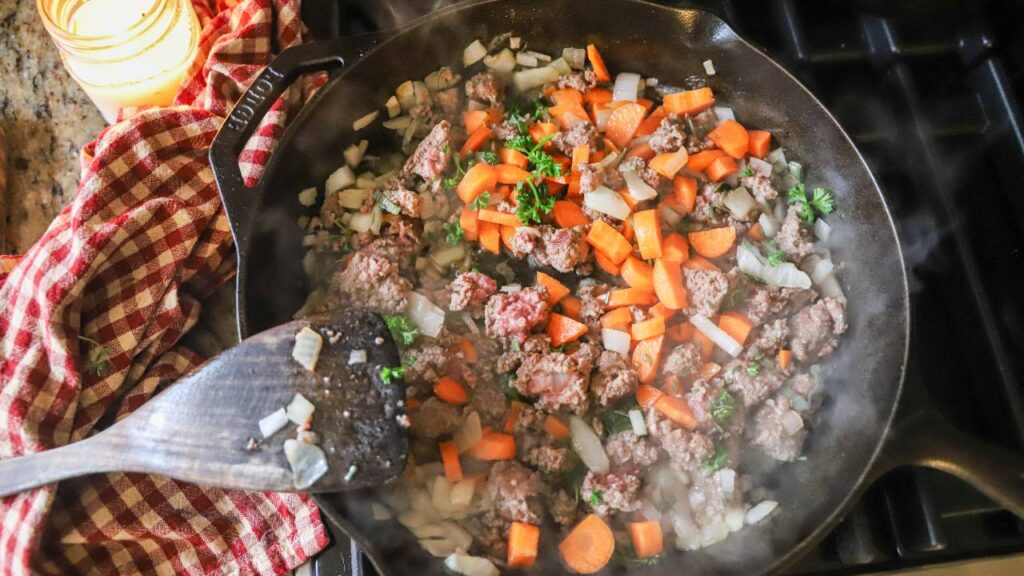 Ground beef, onions, and carrots cooking in cast iron skillet