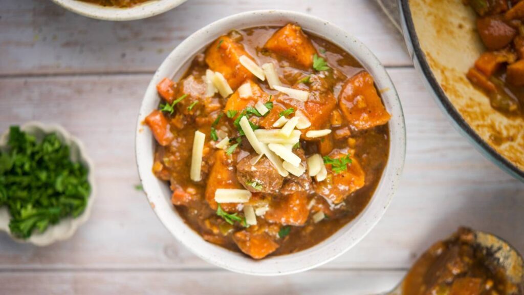 Bowl of pumpkin beef stew with shredded cheese and parsley