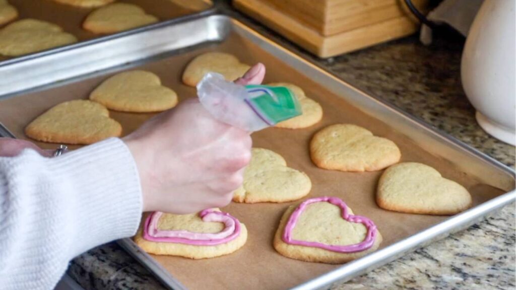 Icing heart-shaped cookies on a baking sheet