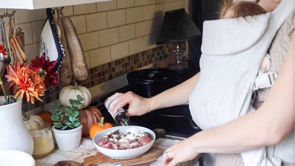 Dredging beef cubes with flour while holding a baby in a carrier