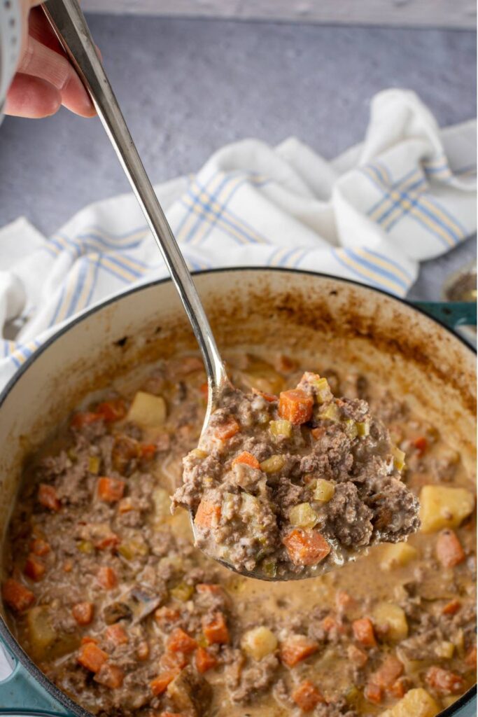 Spoon lifting a scoop of cheeseburger soup from the pot
