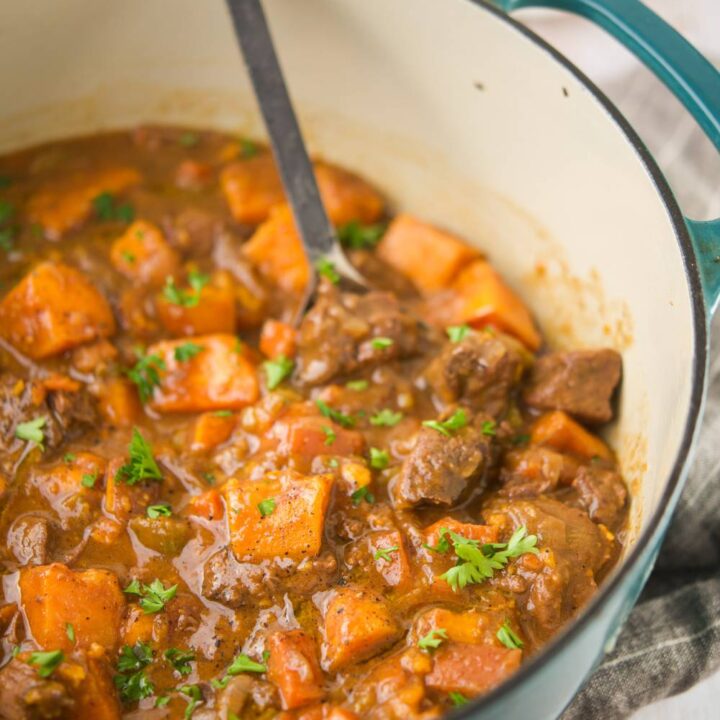 Pumpkin beef stew cooking in a teal Dutch oven with parsley garnish