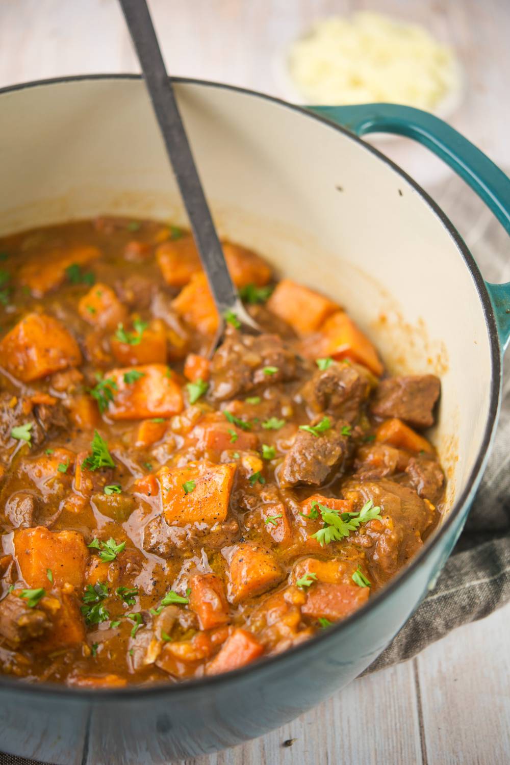 Pumpkin beef stew cooking in a teal Dutch oven with parsley garnish