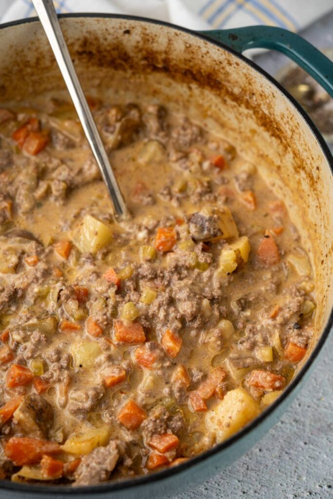 Cheeseburger soup cooking in a Dutch oven with ground beef and vegetables